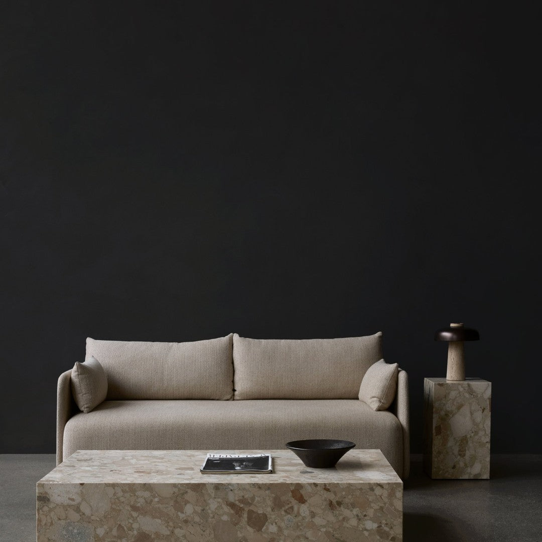 Beige sofa with simple lines, complemented by a textured stone coffee table against a dark backdrop.