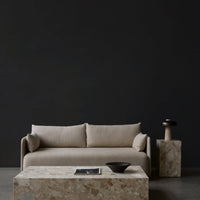 Beige sofa with simple lines, complemented by a textured stone coffee table against a dark backdrop.