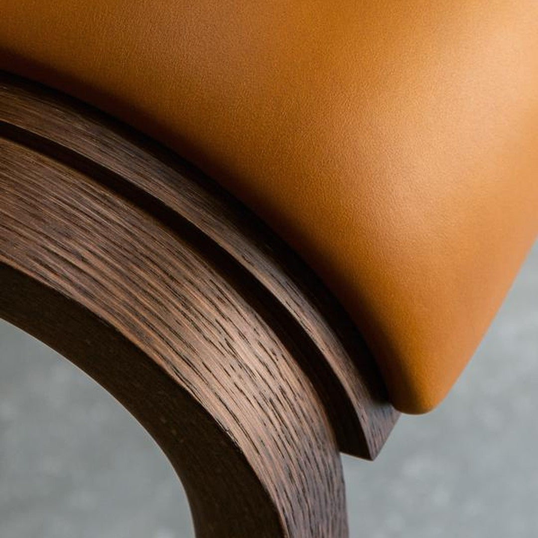 Close-up of a warm brown leather seat with smooth curves and a rich dark wood base, showcasing elegant texture contrast.