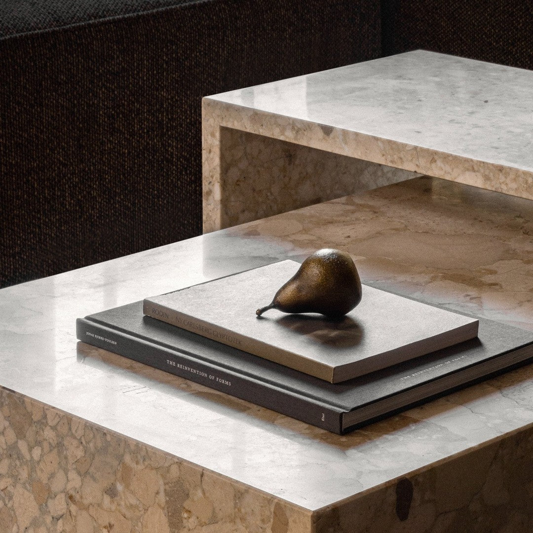 Sleek marble tabletop with beige and brown tones, featuring stacked dark books and a bronze decorative pear.
