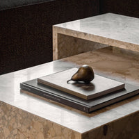 Sleek marble tabletop with beige and brown tones, featuring stacked dark books and a bronze decorative pear.