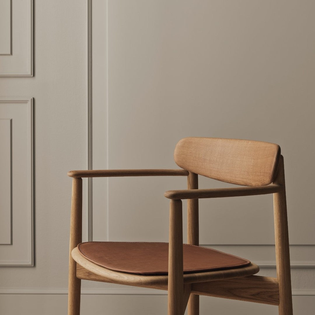 Natural wood chair with a warm brown seat cushion against a soft beige wall and elegant paneling.