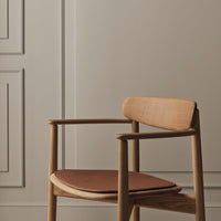 Natural wood chair with a warm brown seat cushion against a soft beige wall and elegant paneling.