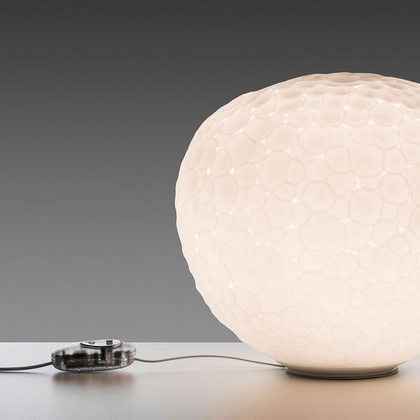 White honeycomb-patterned lamp with soft glow against a gray background, featuring a stylish silver switch.