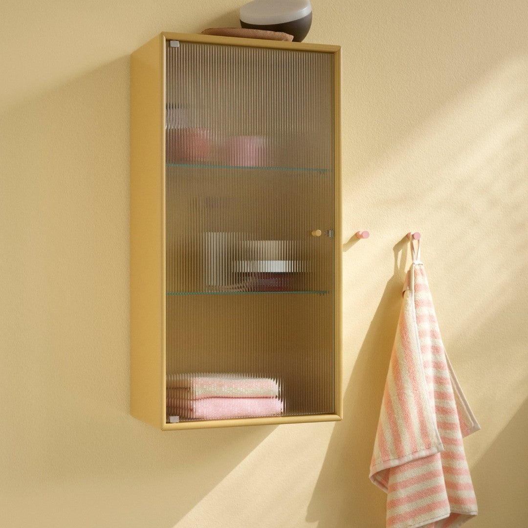 Yellow wall cabinet with glass shelves, showcasing pink towels and a striped towel hanging beside it.