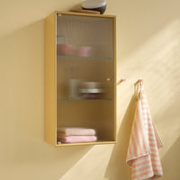 Yellow wall cabinet with glass shelves, showcasing pink towels and a striped towel hanging beside it.