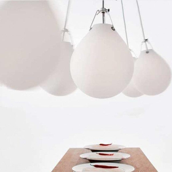 White teardrop pendant lights hanging above a minimalist wooden table with red-accented plates.