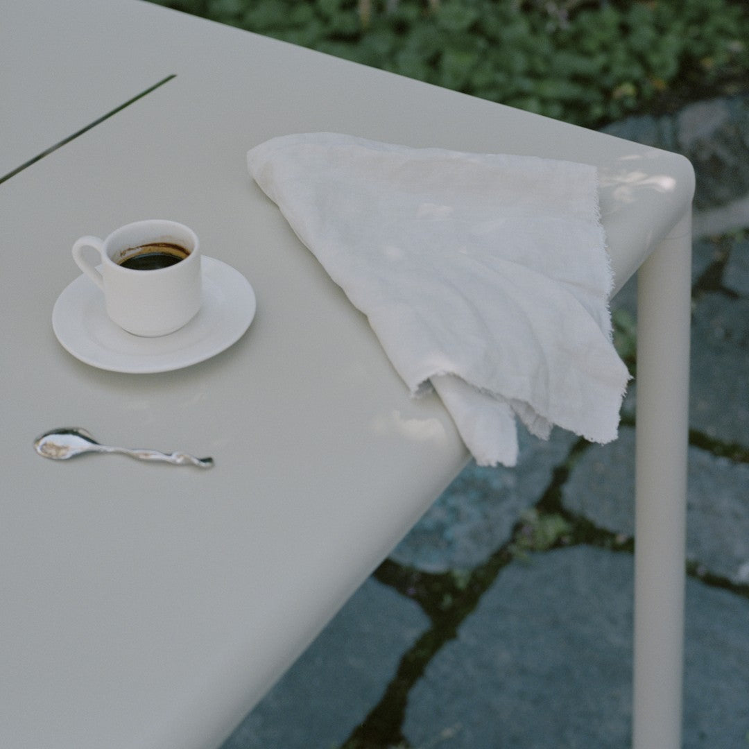 Gray table with a white napkin and cup, featuring a minimalist design against a natural stone background.