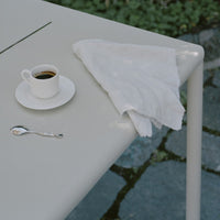 Gray table with a white napkin and cup, featuring a minimalist design against a natural stone background.