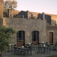 "Outdoor seating with black tables, minimalist design against a rustic gray stone wall and soft greenery."