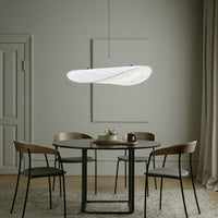 Modern white pendant light above a round black table, complemented by wooden chairs and neutral-toned decor.