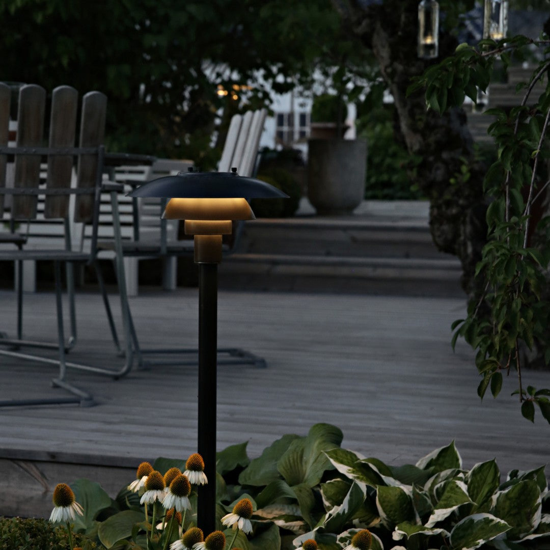 "Elegant black solar light with a gold top, surrounded by lush green plants and vibrant yellow flowers."