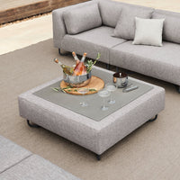 Gray upholstered coffee table with a sleek glass top, paired with soft textures and natural tones.