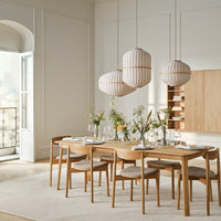 Light wood dining table with beige tones, featuring striped pendant lamps and soft neutral patterns in a modern setting.