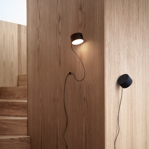 "Modern wall lamp in rich brown and sleek black against a warm wood backdrop, showcasing minimalist design."