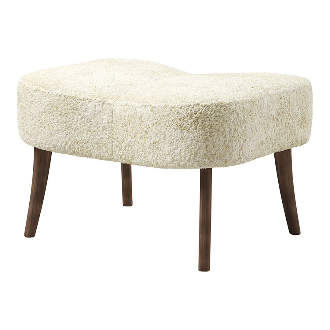 Cream-colored plush ottoman with a unique curved shape and dark wood legs. Ideal for stylish indoor decor.