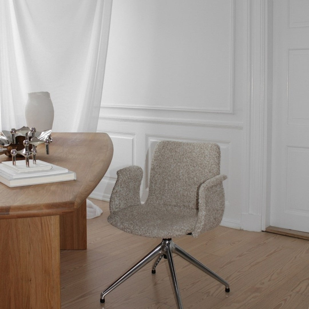 Light gray upholstered chair with soft texture and silver metal base, set against a minimalist wooden desk.