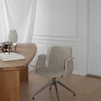 Light gray upholstered chair with soft texture and silver metal base, set against a minimalist wooden desk.