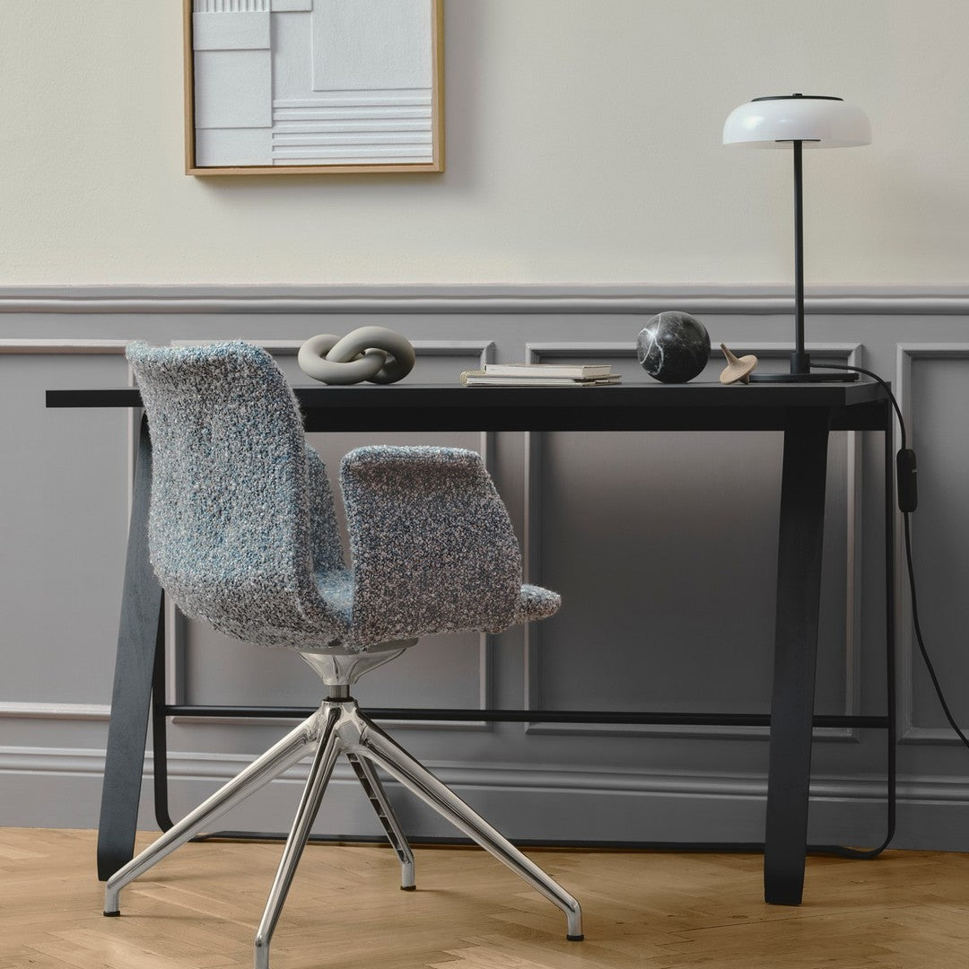 Textured gray chair with colorful speckles, sleek black desk, and minimalistic lamp against light gray wall.