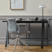 Textured gray chair with colorful speckles, sleek black desk, and minimalistic lamp against light gray wall.