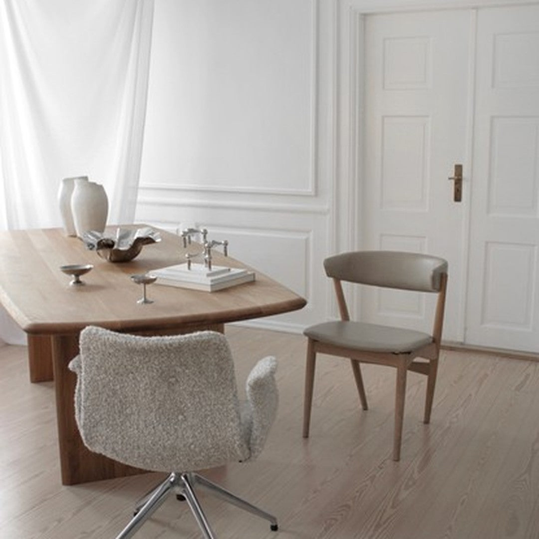 Modern dining room featuring a light wood table, neutral beige chair, and soft textures against white walls.