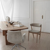 Modern dining room featuring a light wood table, neutral beige chair, and soft textures against white walls.