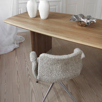 Light wood dining table with a minimalist design, paired with a textured cream chair and subtle white decor elements.