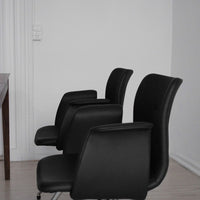 "Modern black leather office chairs with sleek, curved designs on a light wood floor."