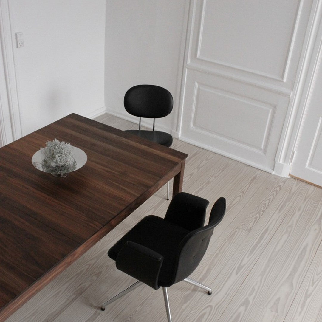 Modern wooden table with a rich brown finish, paired with sleek black chairs against a light wood floor.