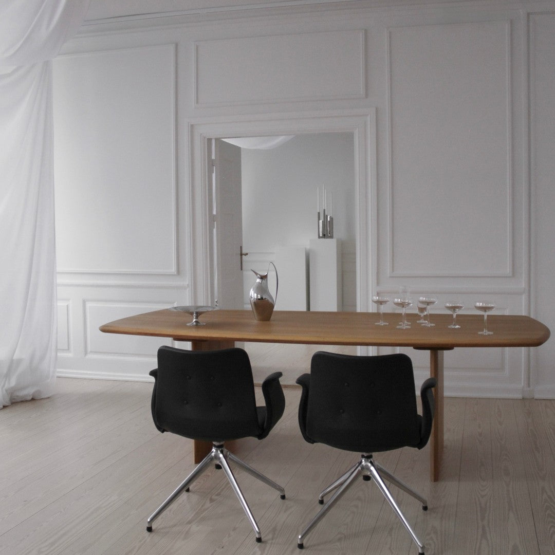 Light wood dining table with black swivel chairs against a neutral, white backdrop. Elegant, minimalist design.
