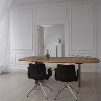 Light wood dining table with black swivel chairs against a neutral, white backdrop. Elegant, minimalist design.