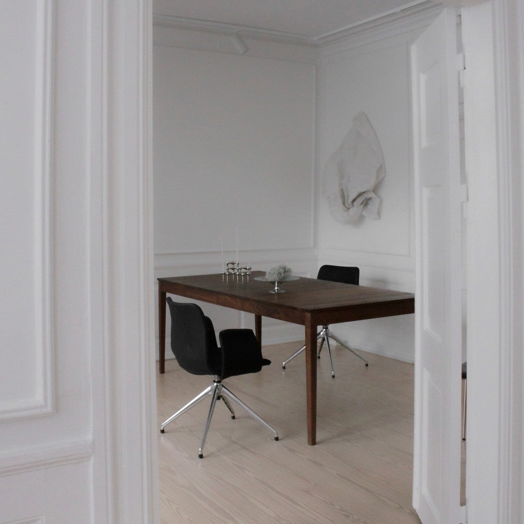 "Modern wooden dining table with black chairs in a minimalist white room, featuring light wood flooring."