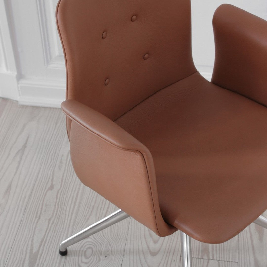 Brown leather chair with button detailing and sleek chrome legs, set against a light wood floor and neutral wall.