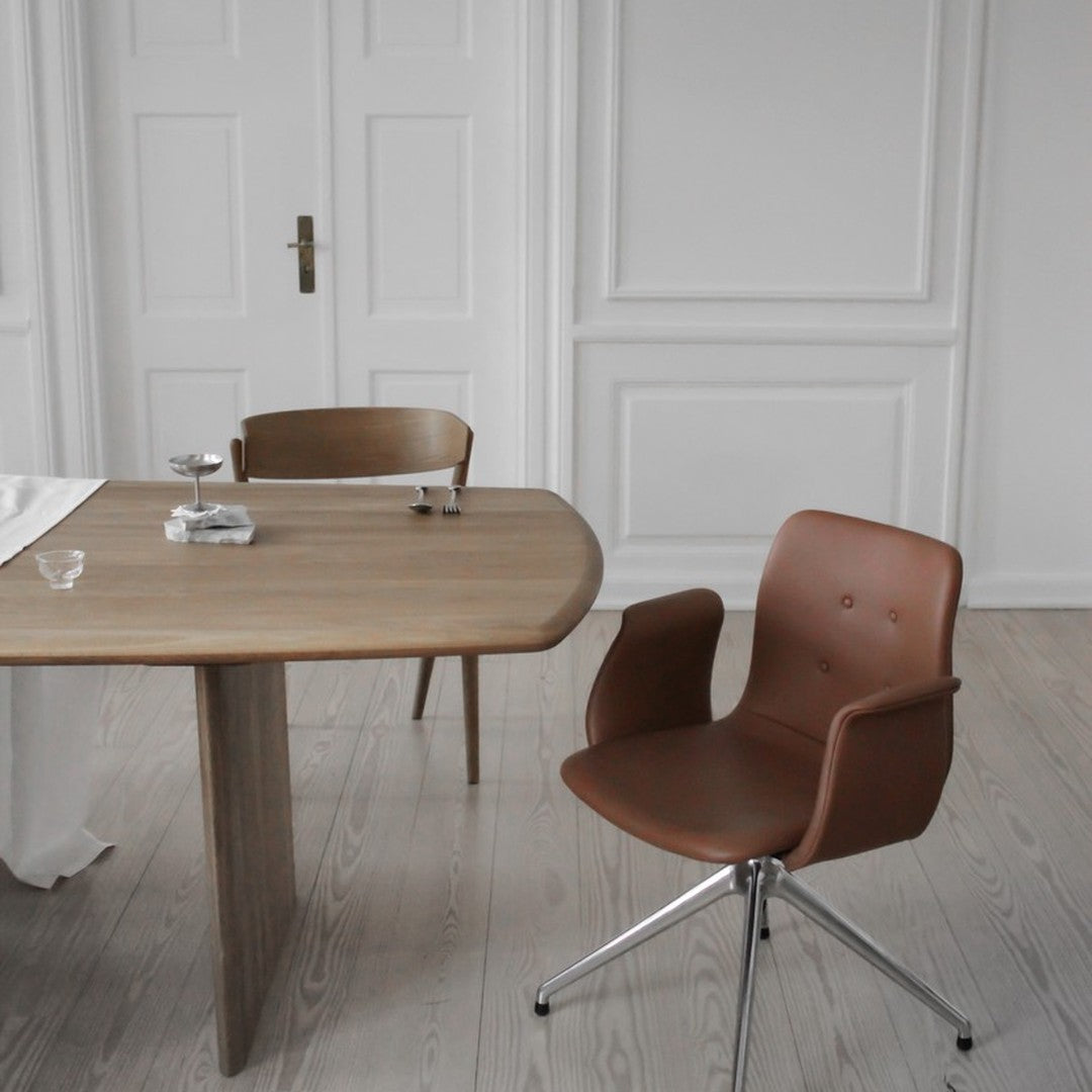 Modern brown chair with sleek lines, paired with a light wooden table in a minimalist, neutral-toned setting.