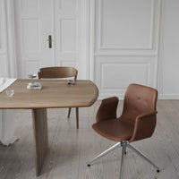 Modern brown chair with sleek lines, paired with a light wooden table in a minimalist, neutral-toned setting.