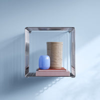 Clear glass shelf with a textured beige vase, a smooth blue vase, and a soft pink book. Bright and modern colors.