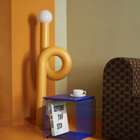 "Bright yellow lamp, blue wire table, and brown checkered couch against an orange backdrop."