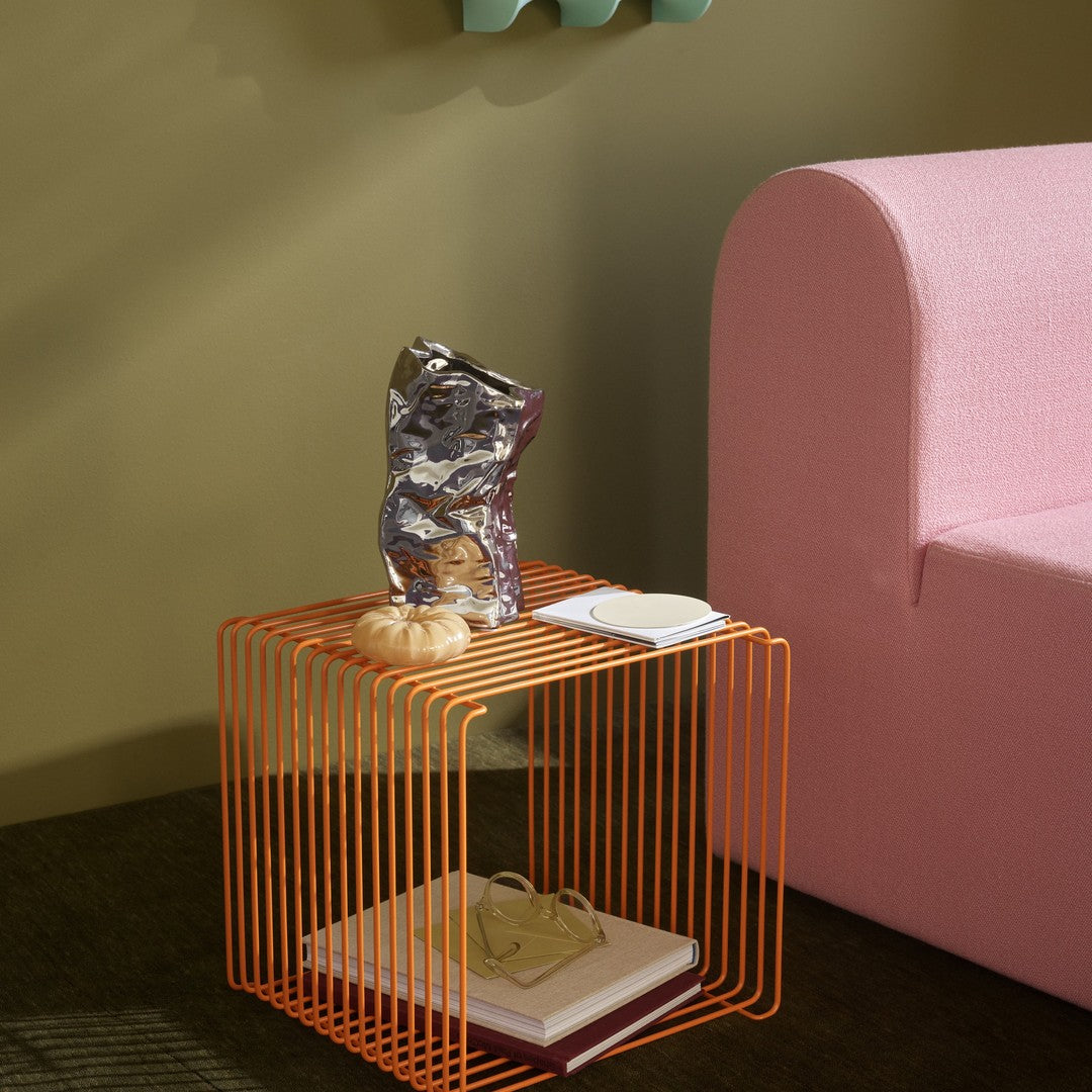 Orange wire cube side table next to a light pink sofa, featuring smooth, modern lines and contemporary design.
