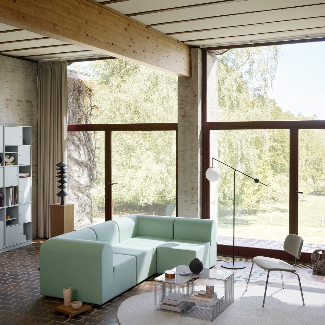 Light mint green sectional sofa with modern lines, set against a natural backdrop of wood and large windows.
