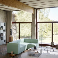 Light mint green sectional sofa with modern lines, set against a natural backdrop of wood and large windows.