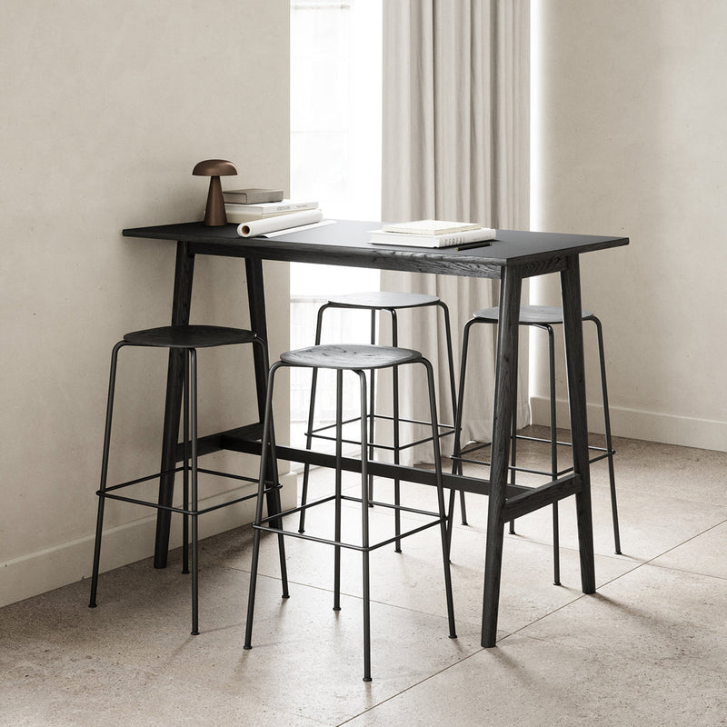 Sleek black bar table with minimalist wire stools against a light beige backdrop and neutral tones.