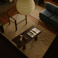 "Modern coffee table with dark wood top and light-colored woven accessories, set on a neutral-toned rug."