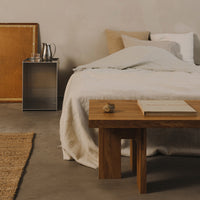 Neutral beige and soft gray bedding with a textured white throw, complemented by warm wood tones and a woven rug.