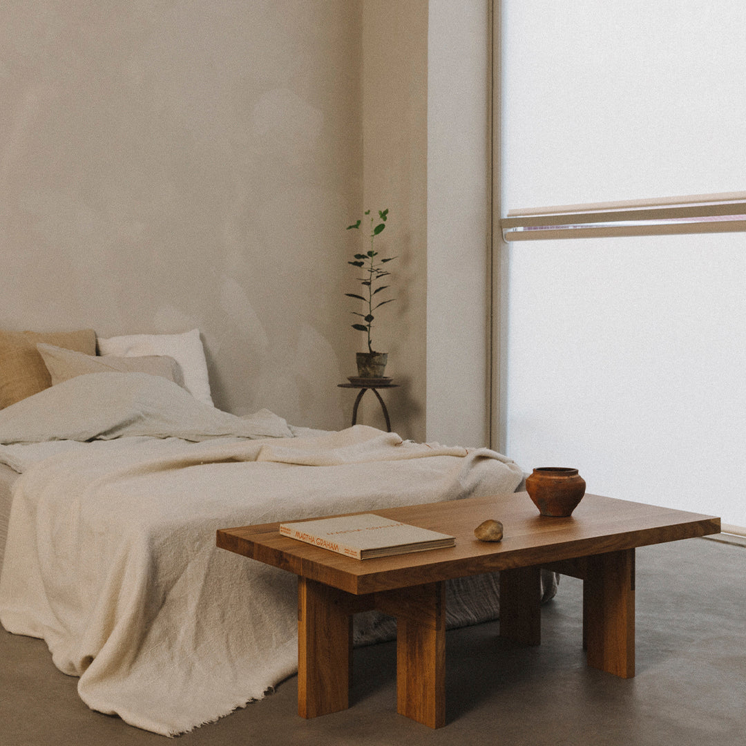Cozy bedroom featuring neutral tones, a textured white blanket, and natural wood accents on a minimalist table.