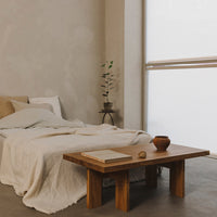 Cozy bedroom featuring neutral tones, a textured white blanket, and natural wood accents on a minimalist table.