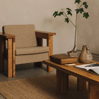 Beige armchair with wooden frame, natural textures, and earthy tones complementing a minimalist interior setting.