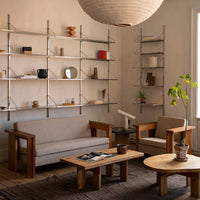 Neutral-toned sofa and chairs with wooden accents, surrounded by a minimalist shelf and soft textures in a bright room.