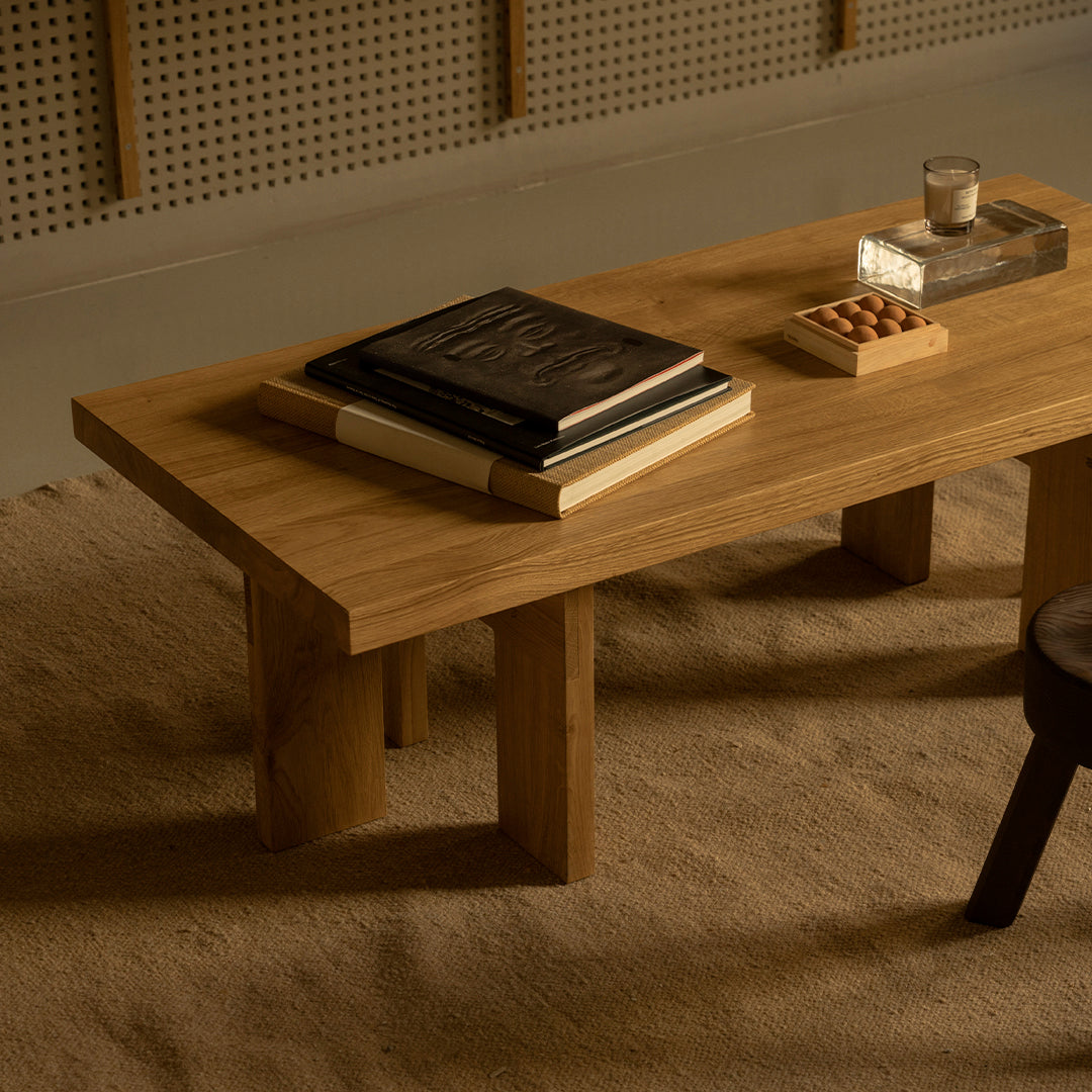 Natural wood coffee table with a smooth surface and light brown finish, set on a textured beige rug.