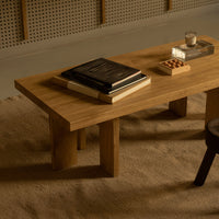 Natural wood coffee table with a smooth surface and light brown finish, set on a textured beige rug.