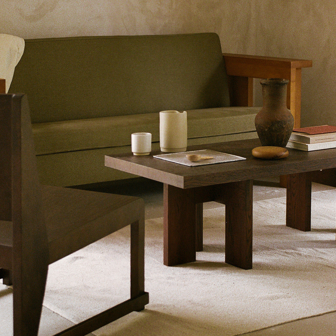 Olive green sofa, dark wooden coffee table, neutral beige rug, and earthy pottery create a warm, inviting interior.